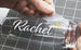 Clear plastic bottle with 'Rachael' printed on it, held by a hand against a grid background.