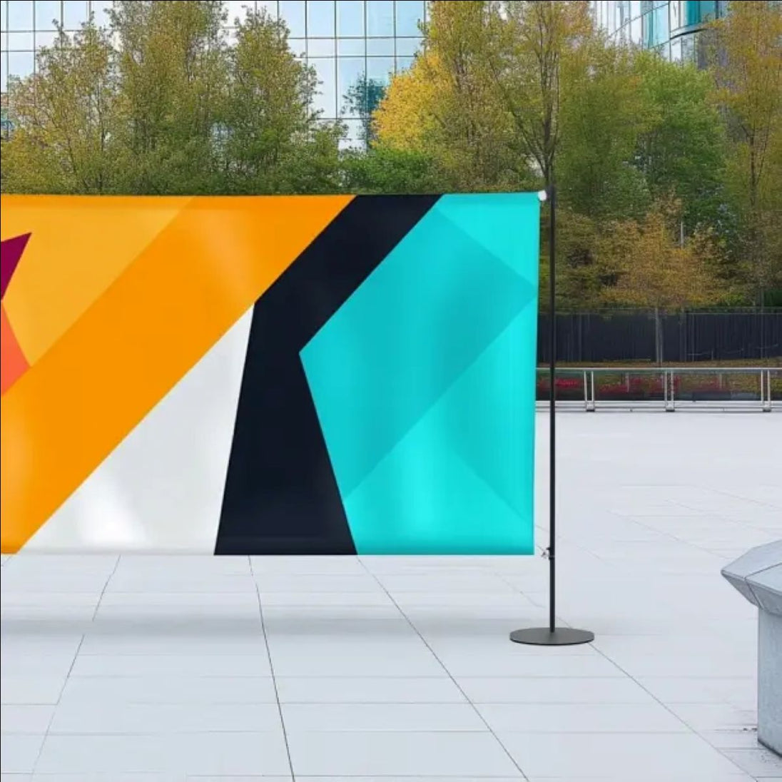 Colorful geometric flag on a stand in an outdoor setting with trees and buildings in the background.