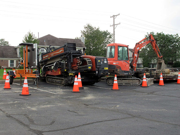 Construction site with excavator and trucks surrounded by traffic cones on a residential street.