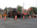 Construction site with excavator and trucks surrounded by traffic cones on a residential street.