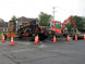 Construction site with excavator and trucks surrounded by traffic cones on a residential street.