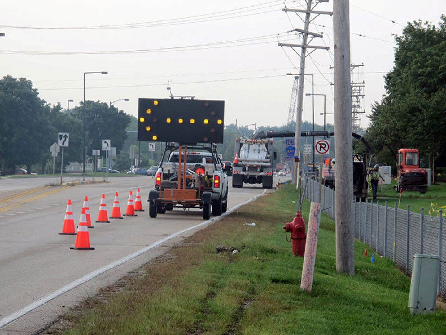 Roadwork scene with traffic cones, construction trucks, and a road sign on a road.