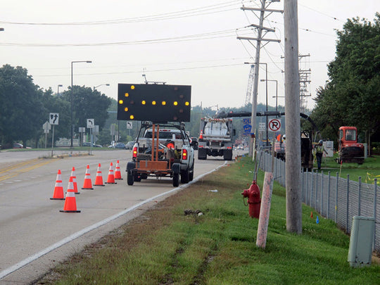 Roadwork scene with traffic cones, construction trucks, and a road sign on a road.