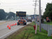 Roadwork scene with traffic cones, construction trucks, and a road sign on a road.