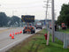 Roadwork scene with traffic cones, construction trucks, and a road sign on a road.