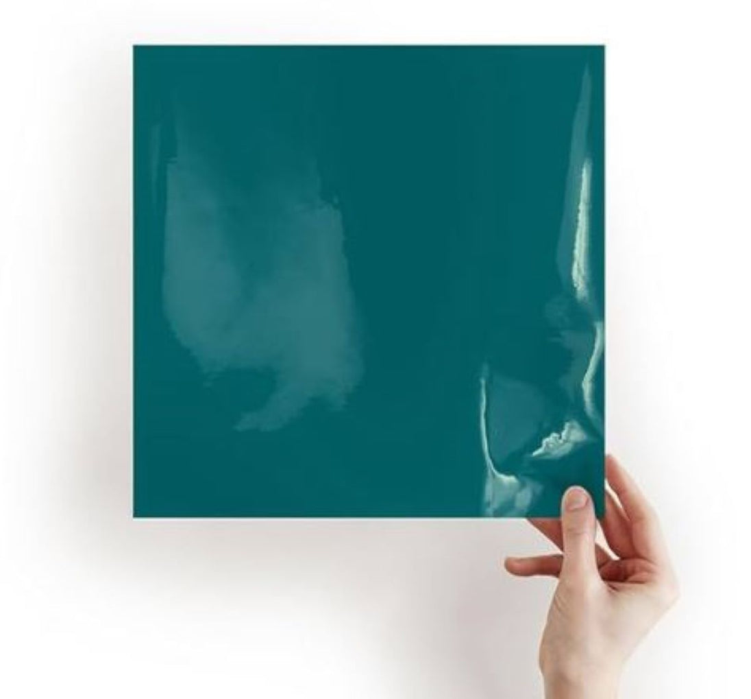 Hand holding a teal-colored square object against a white background