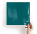 Hand holding a teal-colored square object against a white background
