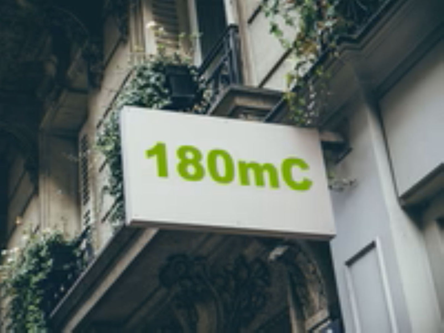 Building facade with a sign displaying '180mC' in green text.