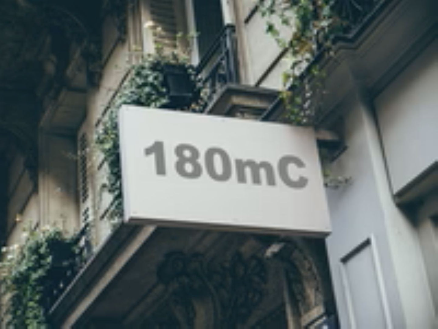 Building facade with a sign displaying '180mC' in pink text.