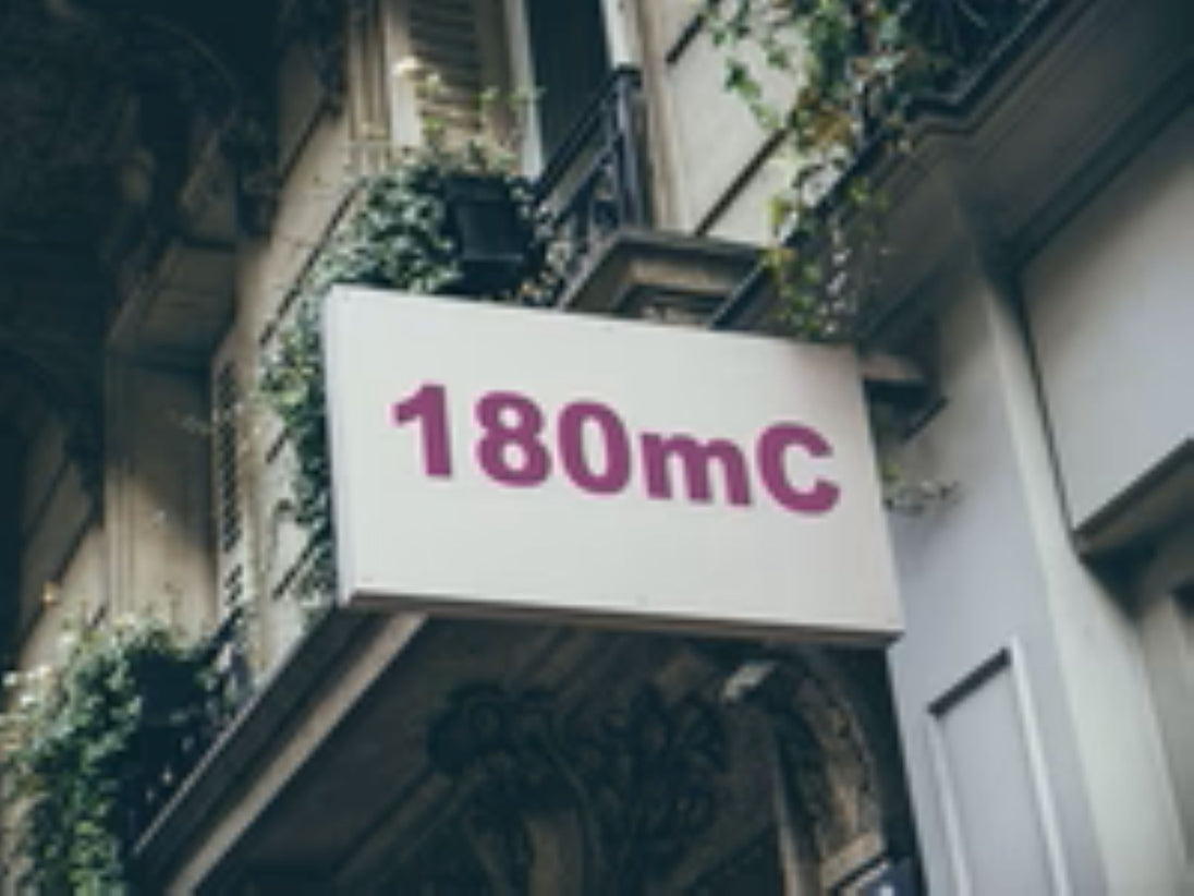 Building facade with a sign displaying '180mC' in pink text.
