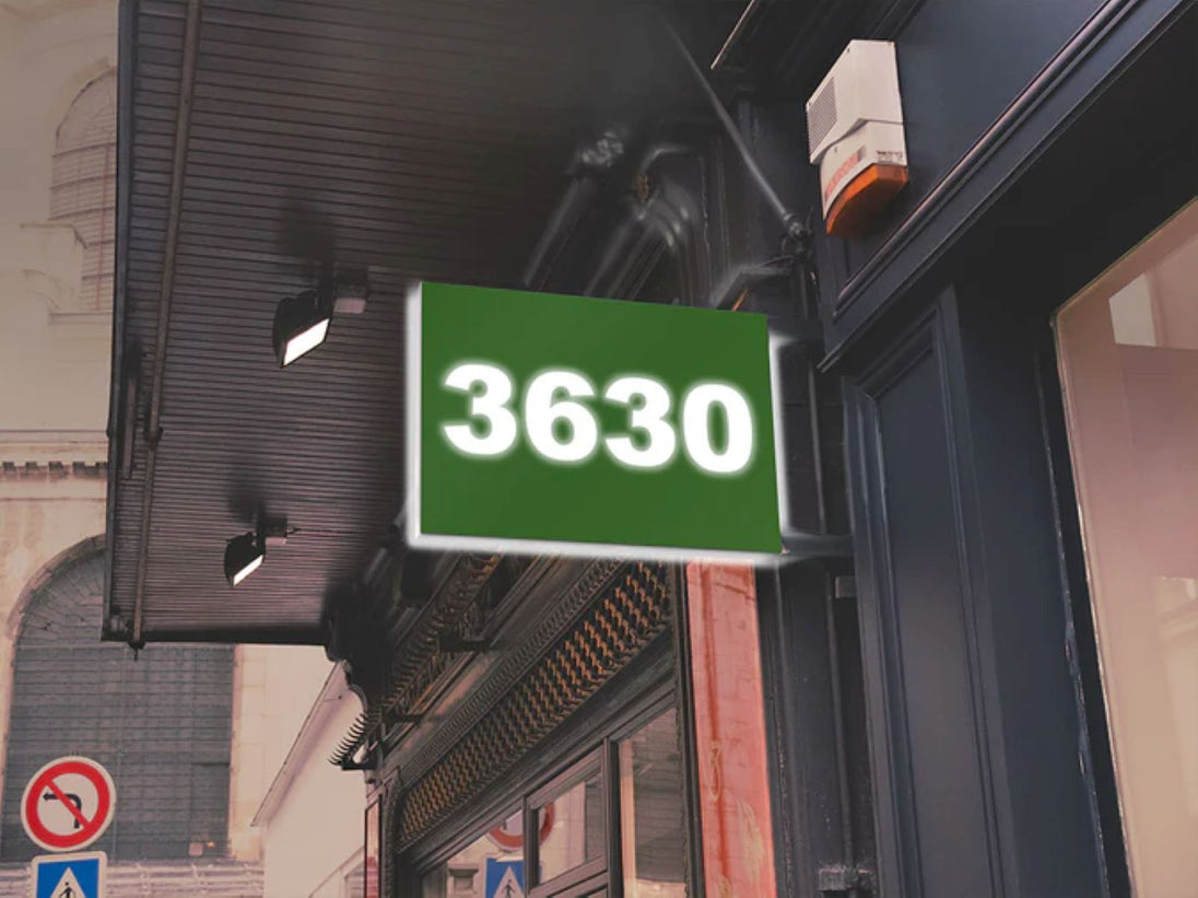 Green sign with the number 3630 on a building facade.
