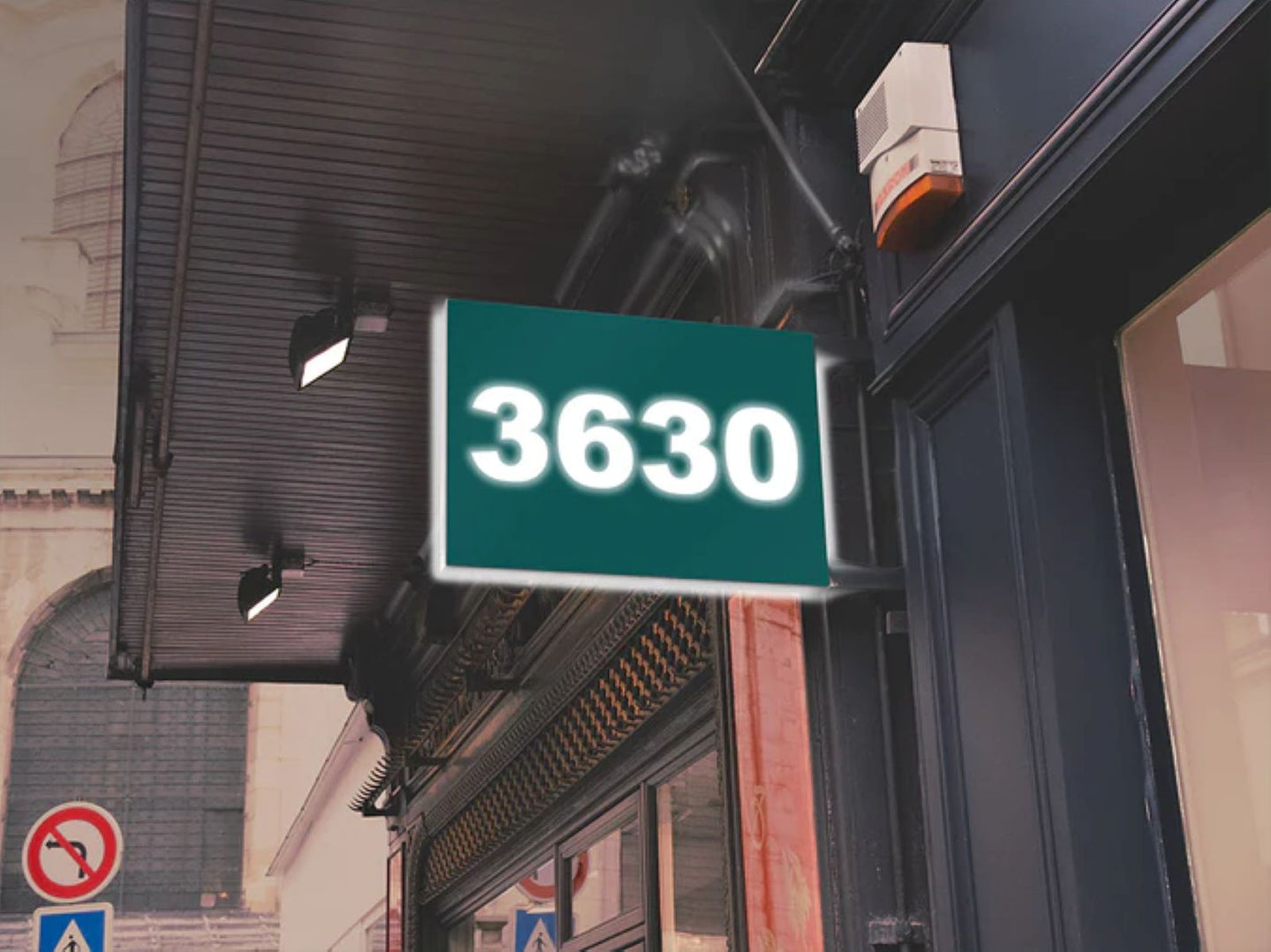 Green sign with the number 3630 on a building facade.