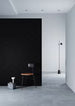 Minimalist interior with a black wall, white floor, and a single chair.