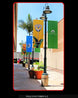 Colorful banners on a lamp post with potted plants and palm trees in the background.