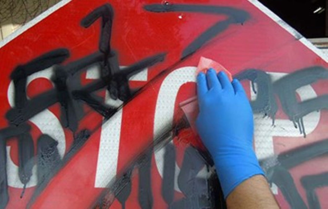 Person cleaning a red and black sign with a sponge and blue gloves
