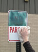 Hand cleaning a 'No Parking' sign with a cloth against a brick wall.