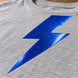 AI application illustration: glossy blue metal-flake-style lightning graphic on gray fabric; representative finish and color.