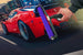 Red sports car with a hand holding a purple and black tool, set against an urban background.