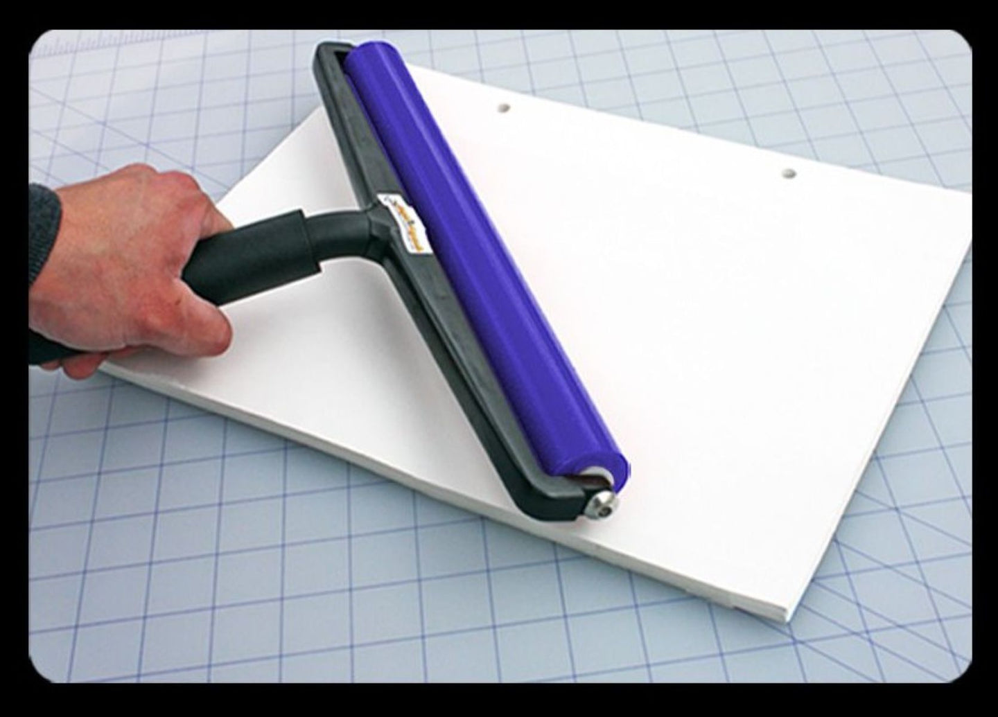 Hand using a squeegee on a white surface with a grid background