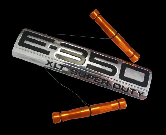 Metallic 'E-650 XLT Super Duty' emblem with orange cylindrical parts on a black background