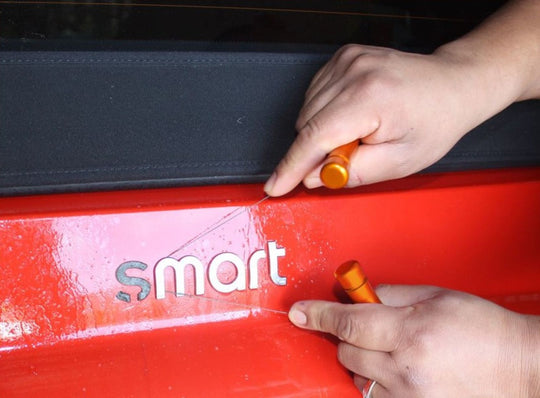Person using a tool on a red vehicle with 'smart' branding.