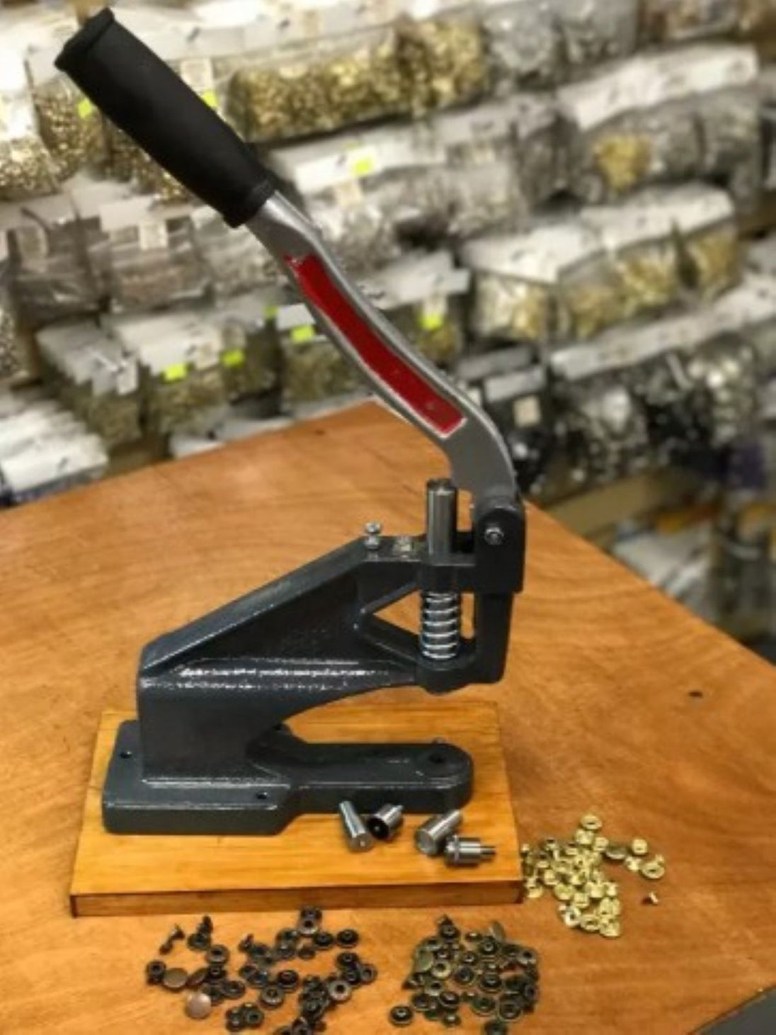 Handheld press tool on a wooden surface with small components in a workshop setting