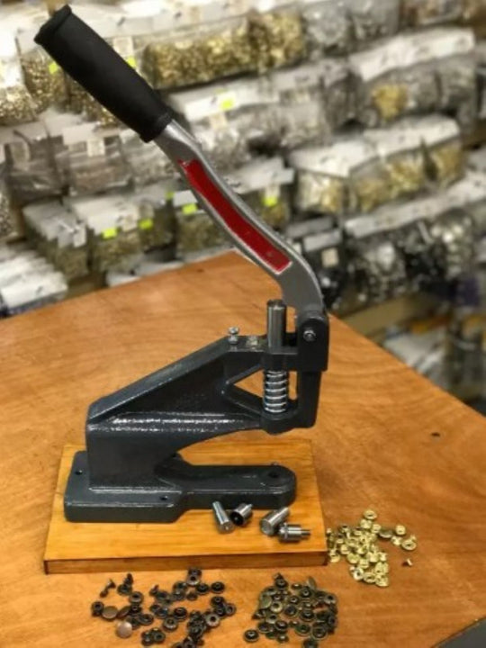 Handheld press tool on a wooden surface with small components in a workshop setting