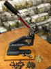 Handheld press tool on a wooden surface with small components in a workshop setting