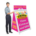 Man holding a pink grand opening sign with colorful balloons and text.