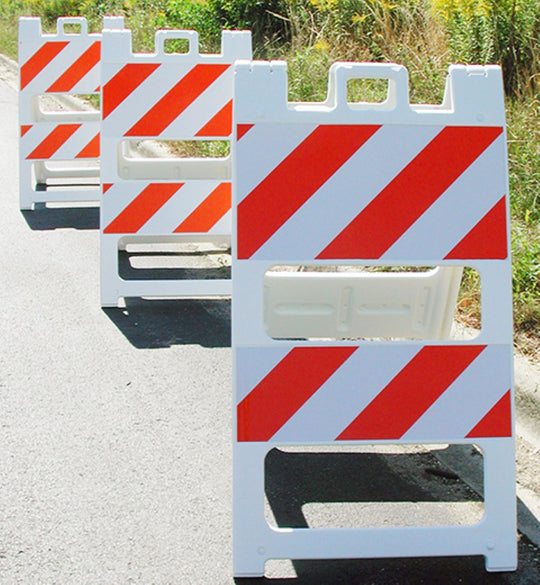 Three road construction barriers with red and white stripes on a road.