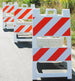 Three road construction barriers with red and white stripes on a road.