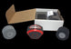 Red and black device with wheels next to an open cardboard box on a black background