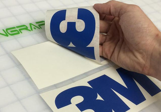 Hand holding a blue and white decal with a grid background