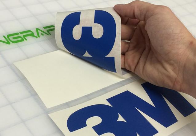 Hand holding a blue and white decal with a grid background