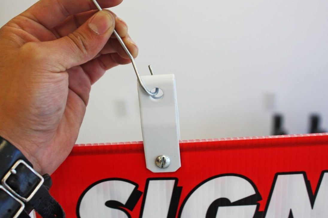 Hand attaching a metal clip to a red sign with 'SIGN' printed on it.