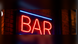 Illustrative red and blue illuminated BAR neon sign in an indoor setting; application illustration for Allanson SS935ICH indoor neon power supply