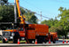 Orange utility truck with crane on a street with traffic cones and trees in the background
