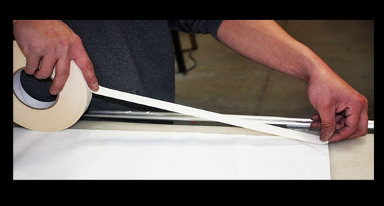 Person applying tape to a long strip of paper or fabric.