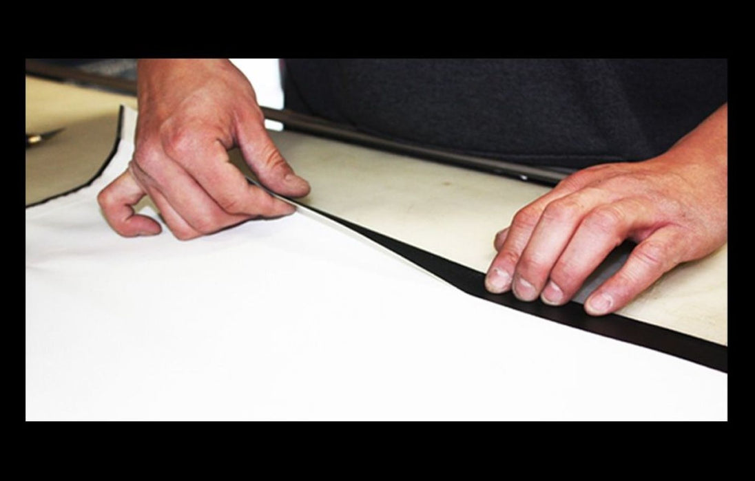 Person applying a strip of black tape or adhesive to a white surface.