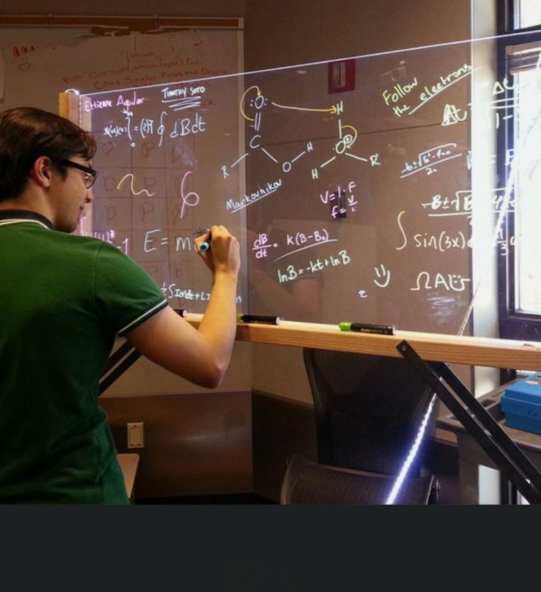 Person writing on a whiteboard with scientific equations and diagrams.