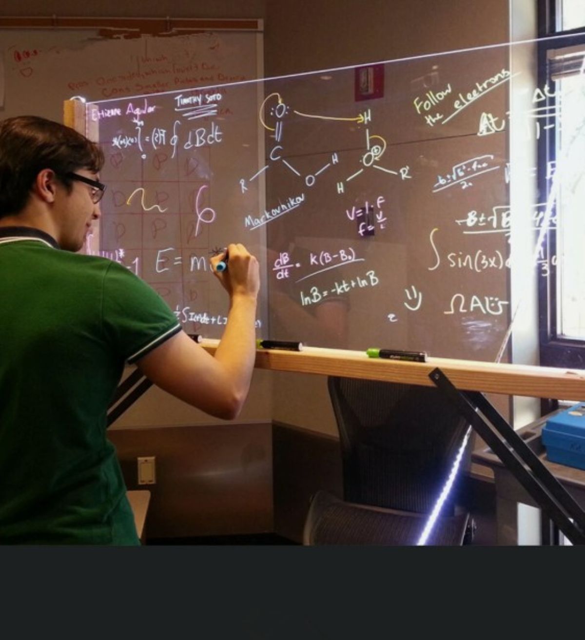 Person writing on a whiteboard with scientific equations and diagrams.