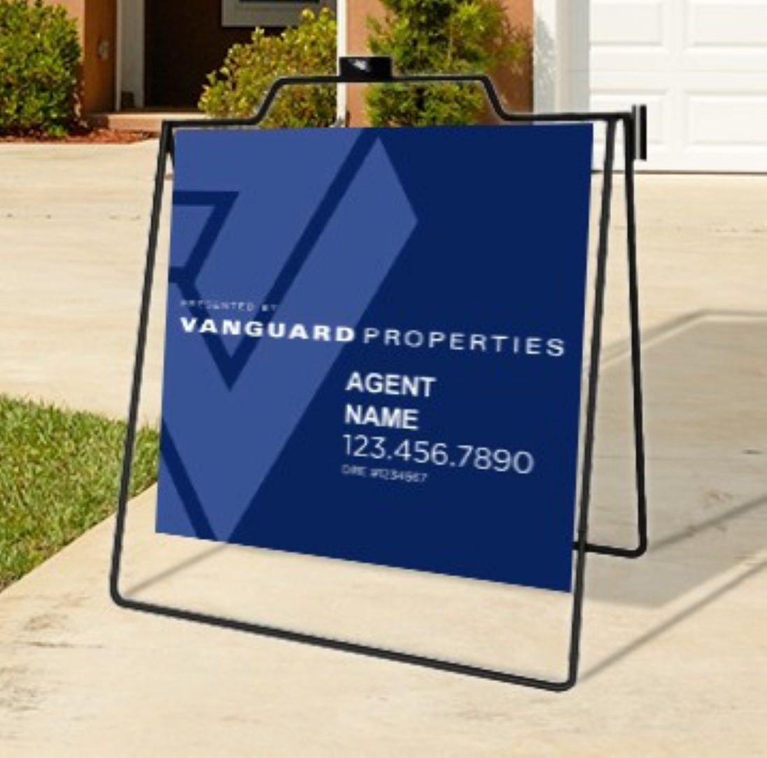 Real estate sign for Vanguard Properties with contact information on a stand outdoors.