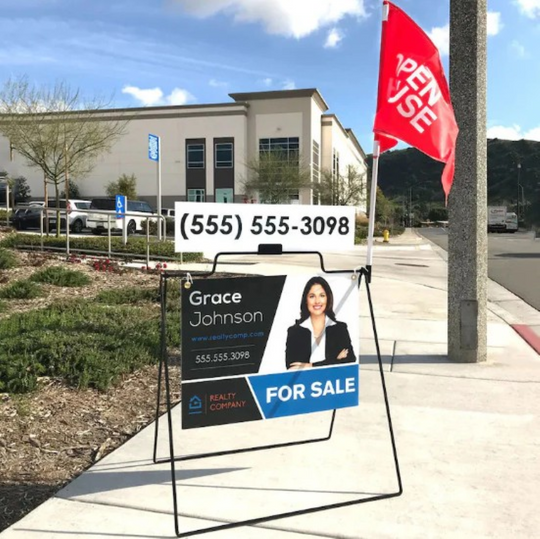 Real estate sign with contact information and 'For Sale' label in front of a building.