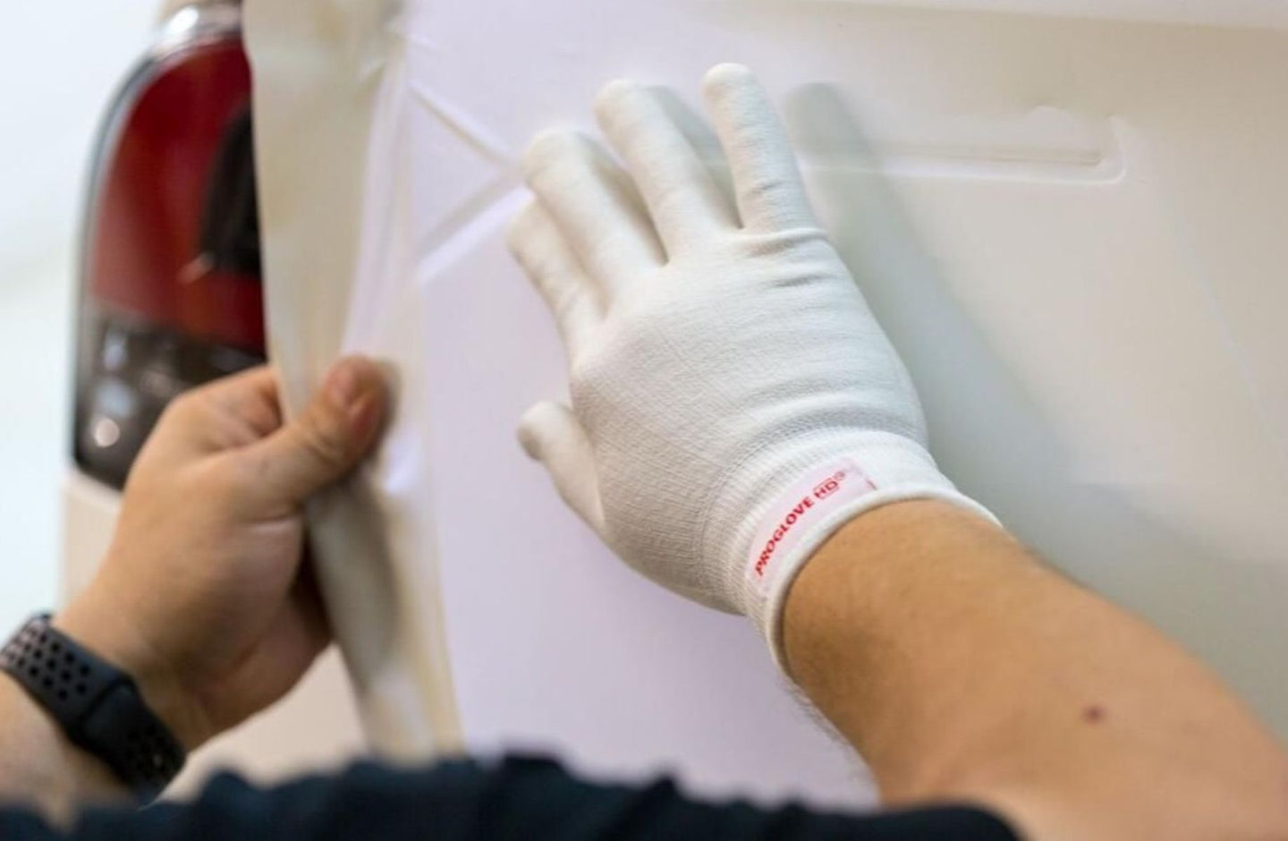 Person wearing a white glove with a red logo, applying a substance to a surface.