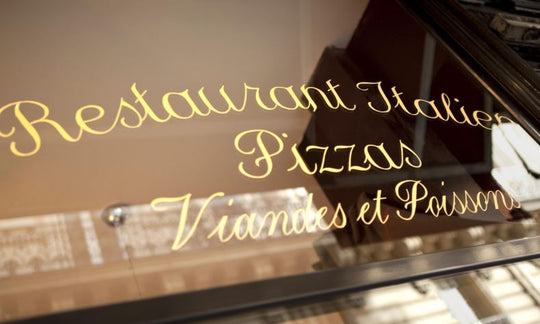Reflective glass window with gold lettering advertising Italian restaurant services.