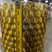 A close-up of a metallic gold textured bucket or planter with a 3D geometric starburst pattern, shown with a measuring tape vertically aligned on the front to indicate its height.