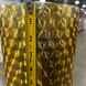 A close-up of a metallic gold textured bucket or planter with a 3D geometric starburst pattern, shown with a measuring tape vertically aligned on the front to indicate its height.