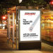 A tall outdoor LED sign display at a bus stop at night, showing a promotional ad for SIGN HERO LED Sign Lights with text and a graphic of a light fixture.