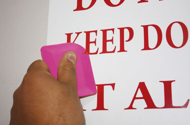 Hand holding a pink object against a white background with red text.