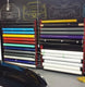 Rolls of vinyl wrap in various colors on a rack with car designs in the background.